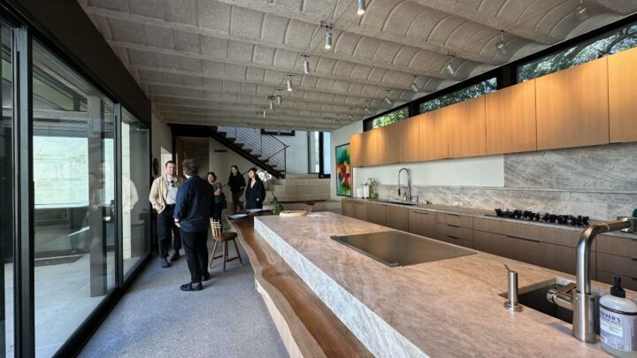 Modern kitchen with marble island, wooden cabinets, and people exploring the stylish op...