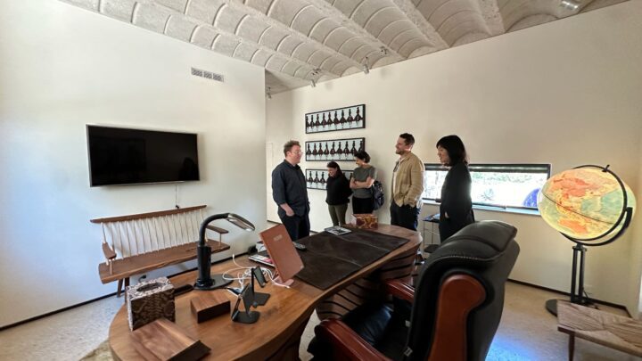 Michael Ellsworth, Evan Morris, and Vicki Yuan chatting in the stylish office of Lake Flato's Olmos Park Residence with modern decor, wooden desk, and illuminated globe.
