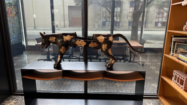 Wooden animal sculpture with cloud patterns on a black shelf, placed by a window in a c...