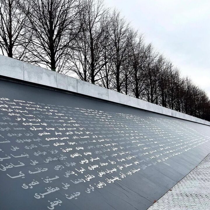 Wall with engraved text in Arabic script, aligned with leafless trees against a cloudy ...