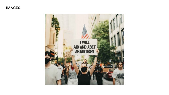 Protester holding I Will Aid and Abet Abortion sign at a rally in a city street, wearin...