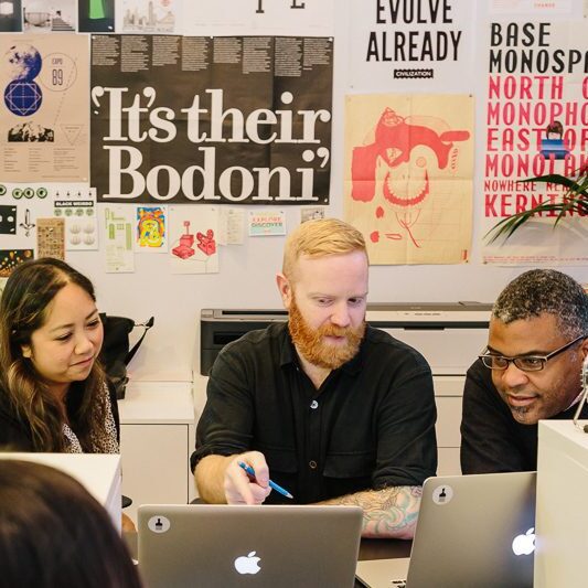 Team collaborating in a modern office, surrounded by design posters, working on laptops.