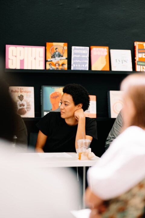 Person sitting at a table in a bookshop, surrounded by colorful books on display.