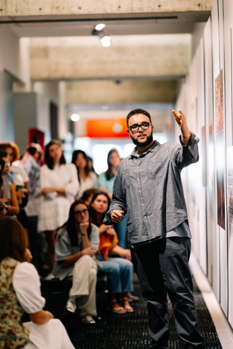 Man giving a presentation in a gallery, engaging an attentive audience.