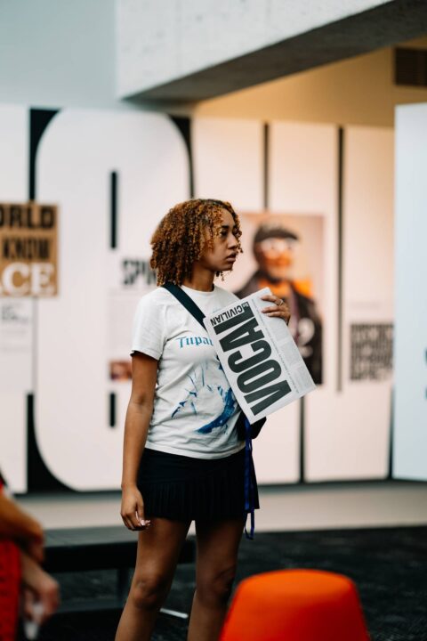 Young woman holding a printed artwork in a modern gallery, with posters on display in t...