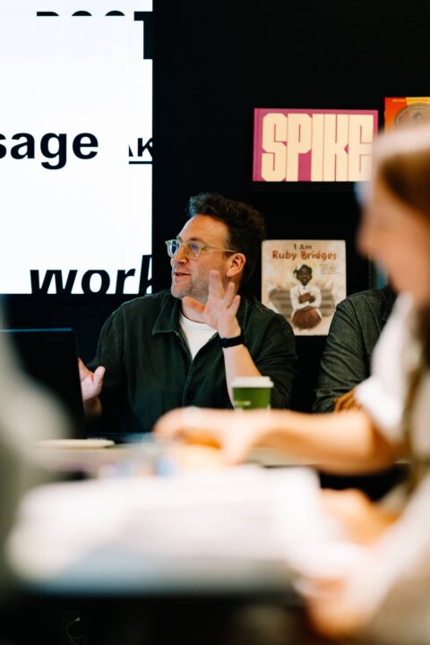 Man giving a presentation in a meeting room with books on the background.