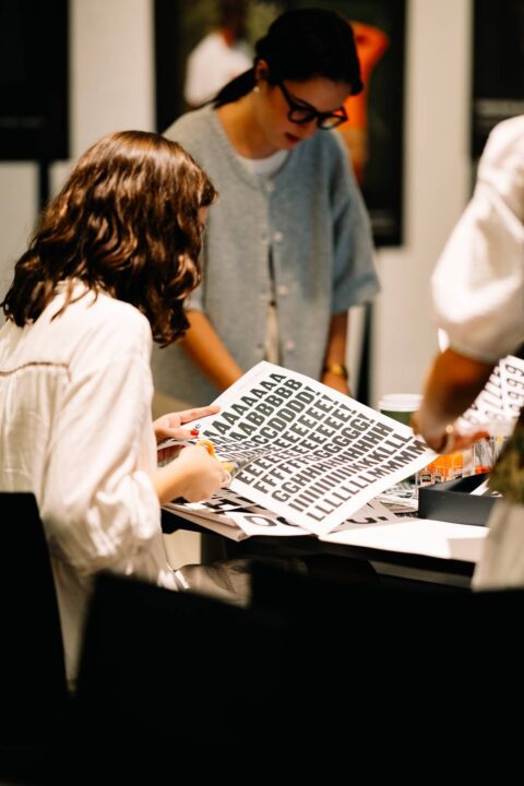 People collaborating on a typography project, examining and cutting black letter sheets...