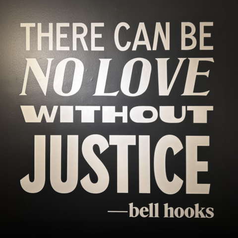 Quote on a black wall: There can be no love without justice. - bell hooks. Bold white text emphasizing social justice and love.