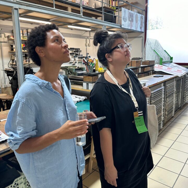 Two people observing a creative workspace, surrounded by art supplies and posters.