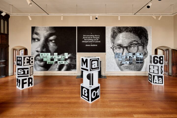 Art installation with large portraits, cube structures, and a James Baldwin quote on ch...