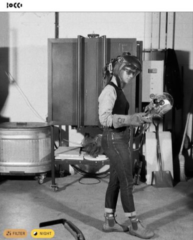 Person in protective gear examines a glass skull in an industrial workshop setting.