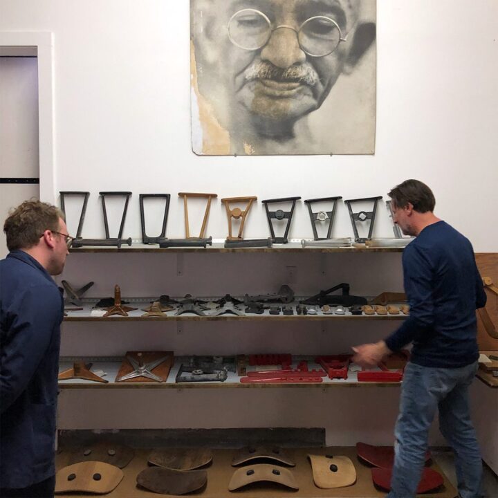 Two individuals examining vintage chair components on shelves, with a large portrait above.