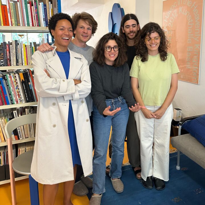 Raya Leary with a group of lecture attendees indoors, standing near a bookshelf with colorful books in a cozy room setting at Bikini Books in Porto Portugal.