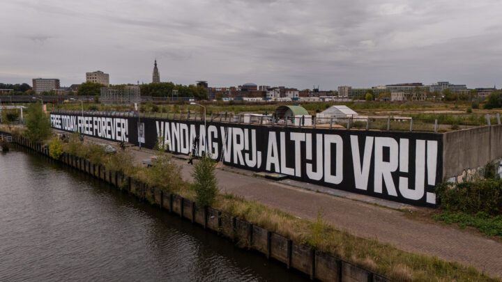 Large mural along a canal showing bold text: Free today, free forever! in English and D...